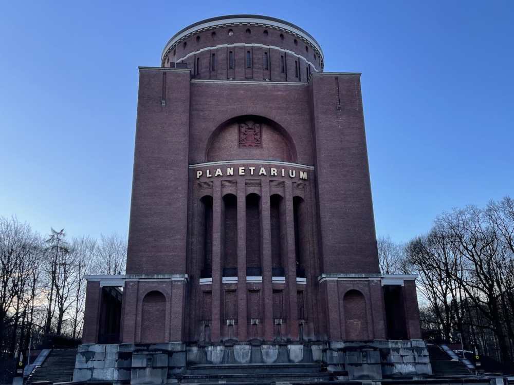Monumental Art Deco brick facade of Planetarium Hamburg with tall vertical windows, decorative crest, and ‘PLANETARIUM’ signage, framed by leafless winter trees under a clear blue winter sky.