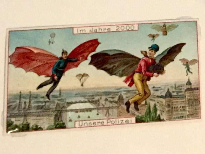 Vintage German postcard showing two policemen with bat-like wings flying above a city; caption reads “Our police in the year 2000".