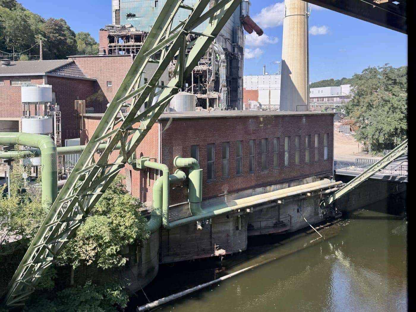 Historic industrial brick factory building with green pipes bordering the Wupper river, seen from the Wuppertal suspension railway.